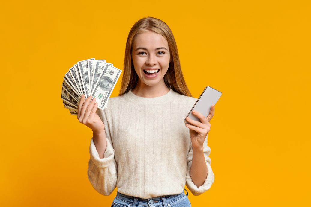 Happy teen girl showing holding smartphone and bunch of money
